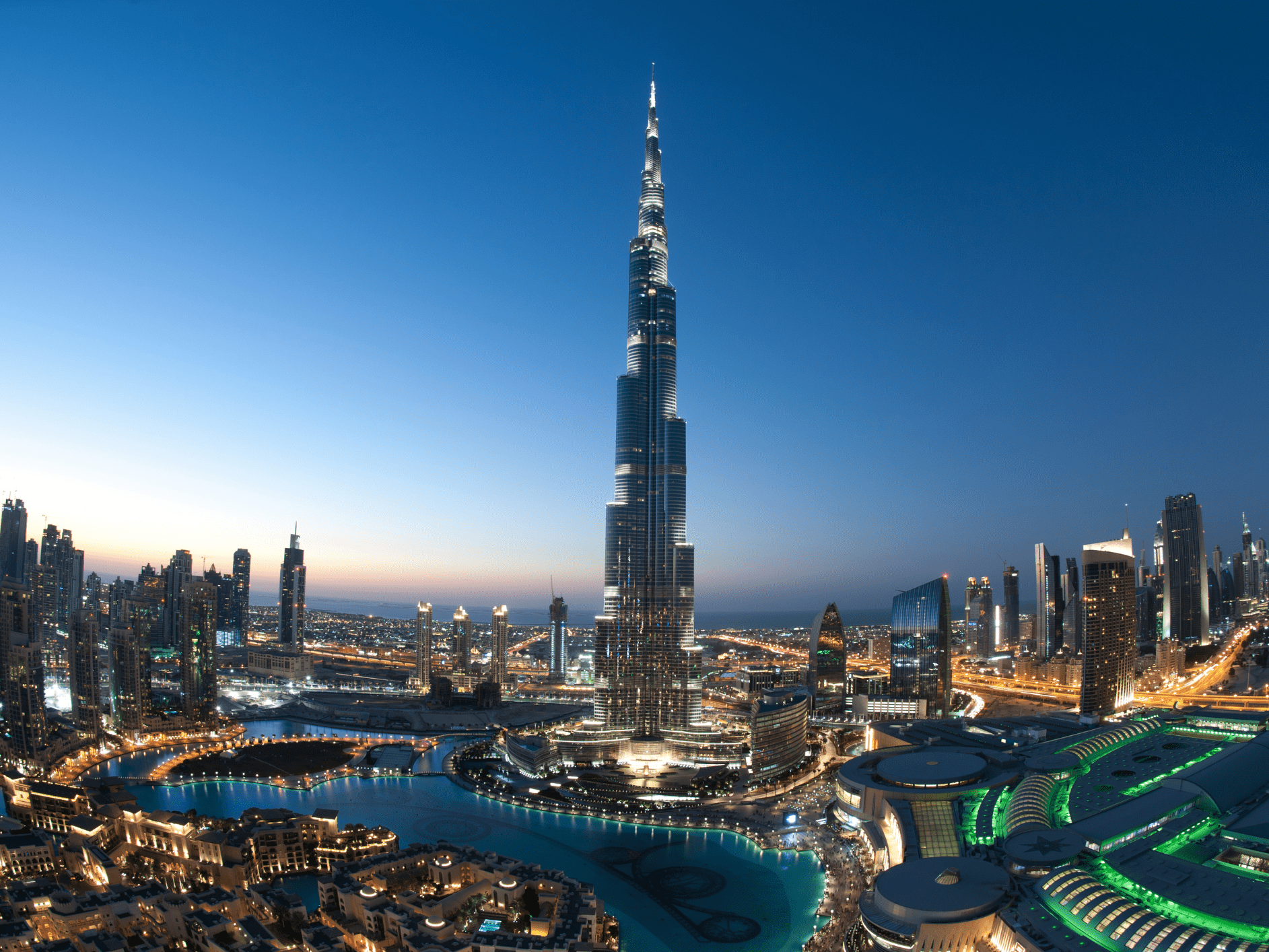 Burj Khalifa towering over Dubai skyline at dusk, with illuminated skyscrapers and a winding waterfront below